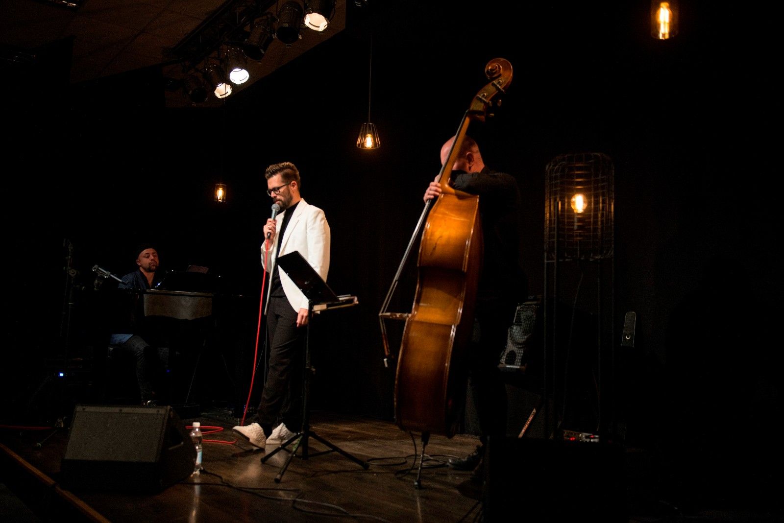 Trio Michała Bobera, pianista i kontrabasista w czarnych strojach, Michał Bober w białej marynarce