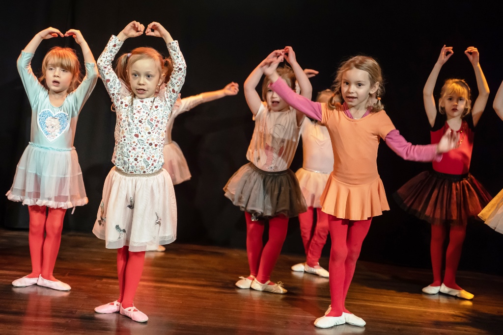*pięć małych dziewczynek w baletkach stoi na scenie z uniesionymi w kolistym kształcie rękami nad głową